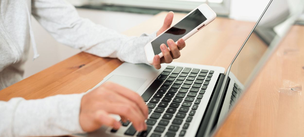 Detail na ruce muže pracujícího na notebooku v levé ruce drží telefon