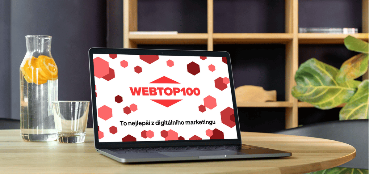 Na notebooku logo web top 100. Notebook na stole, vedle položená sklenice vody