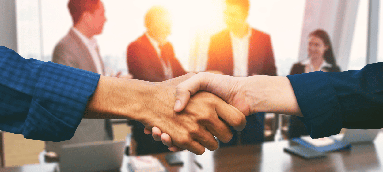 Detail na podání rukou, v pozadí zasedací místnost plná lidí