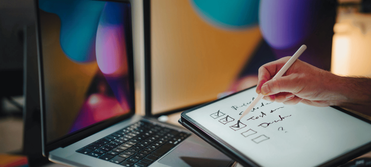 osoba sedící u počítače odškrtávájící si na papíře hotové úkoly.